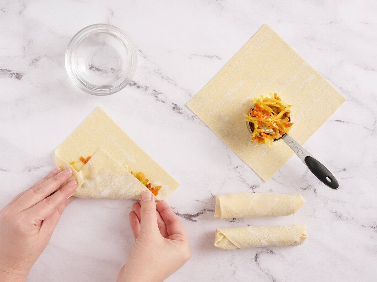 A hand rolling vegetable egg rolls.