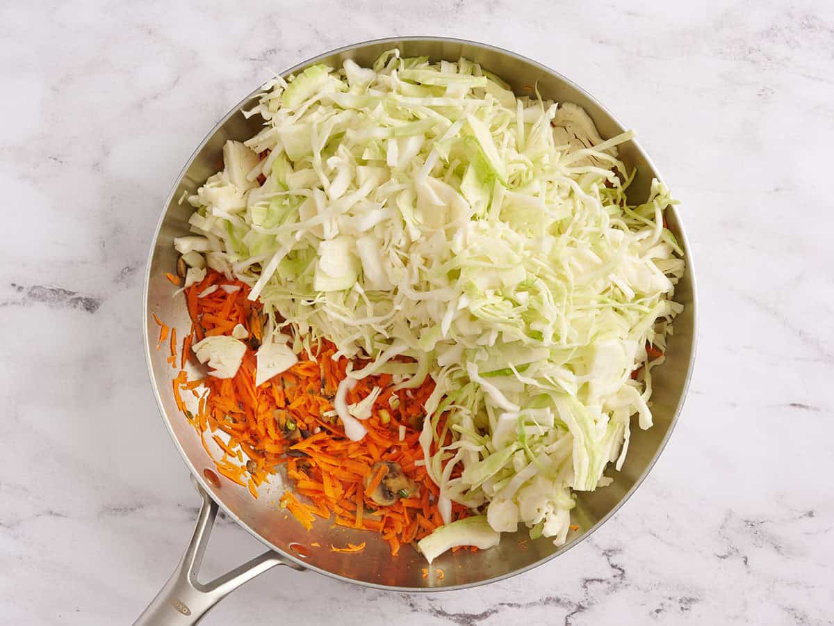 Shredded cabbage in a skillet with sauteed vegetables.