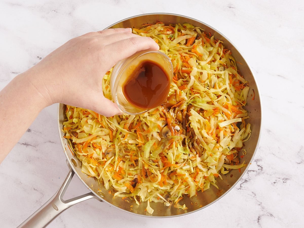 Thickened soy sauce being poured into a skillet of sauteed vegetables.
