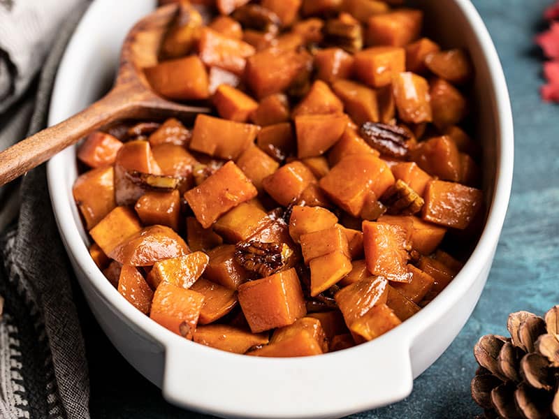Maple Roasted Sweet Potatoes with Pecans (aka Candied Yams) are an easy, classic Thanksgiving side dish that everyone will love. BudgetBytes.com Front view of the casserole dish full of Maple Roasted Sweet Potatoes with Pecans with pine cones on the side