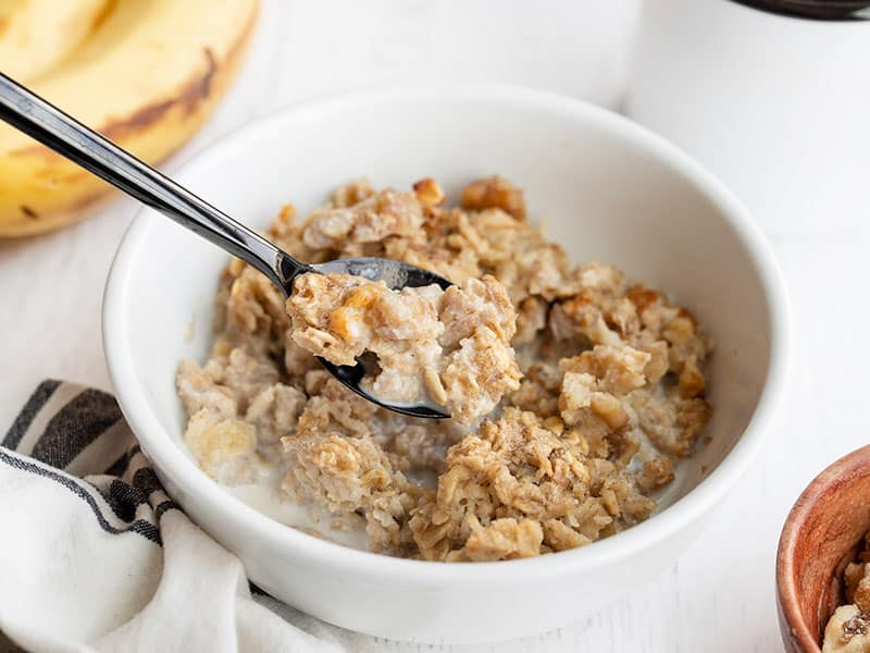 The rich and sweet flavor of banana bread infused into a healthy baked oatmeal. This Banana Bread Baked Oatmeal is perfect for breakfast meal prep! Budgetbytes.com Side view of a bowl of banana bread baked oatmeal with a spoon lifting a bite