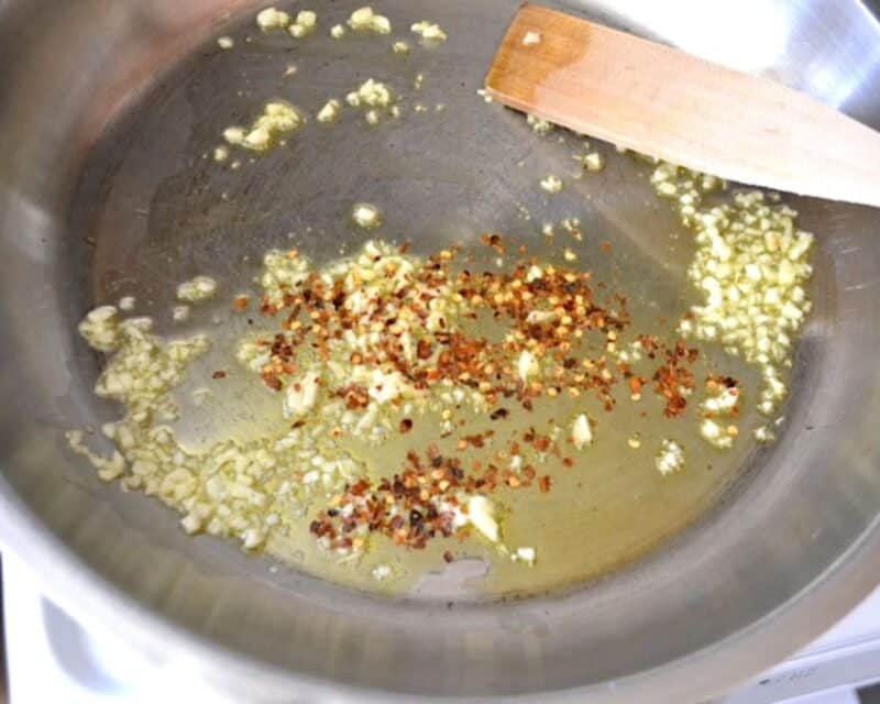 Adding crushed red chili flakes to the olive oil with the garlic.