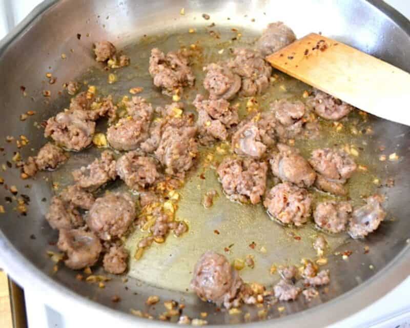 Cooking the sausage in a pan with a wooden spoon.