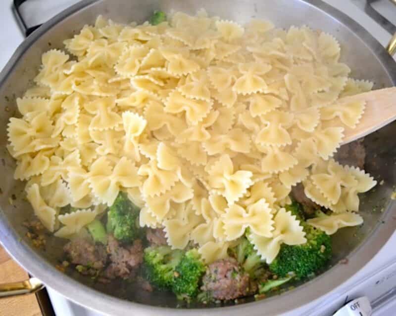 Adding bowtie pasta to the skillet with the broccoli and sausage.
