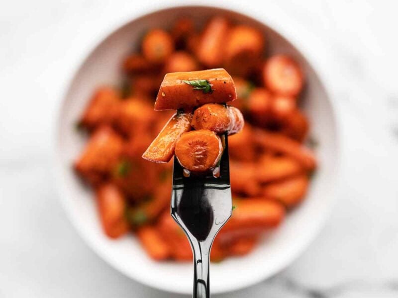 Honey Balsamic Glazed Carrots are a simple but delicious side dish that is easy enough for busy weeknights, but fancy enough for company! Budgetbytes.com close up of a forkful of honey balsamic glazed carrots with the bowl in the background