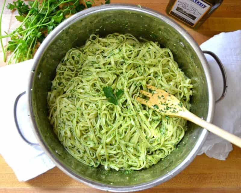 Pasta coated with pesto in a pot with a wooden spoon.