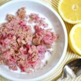 Creamy lemon raspberry oatmeal in a bowl with a spoon and lemons.
