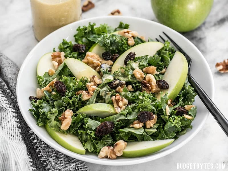 This Apple Dijon Kale Salad is tangy, sweet, and crunchy with Granny Smith apples, walnuts, raisins, and a homemade Dijon vinaigrette. BudgetBytes.com A bowl of Apple Dijon Kale Salad from the front