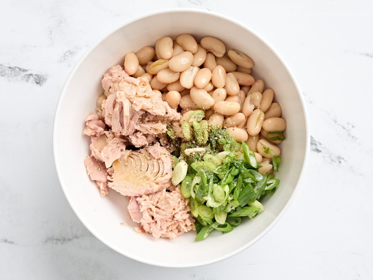 White beans, canned tuna, sliced green onions, and seasonings in a bowl.