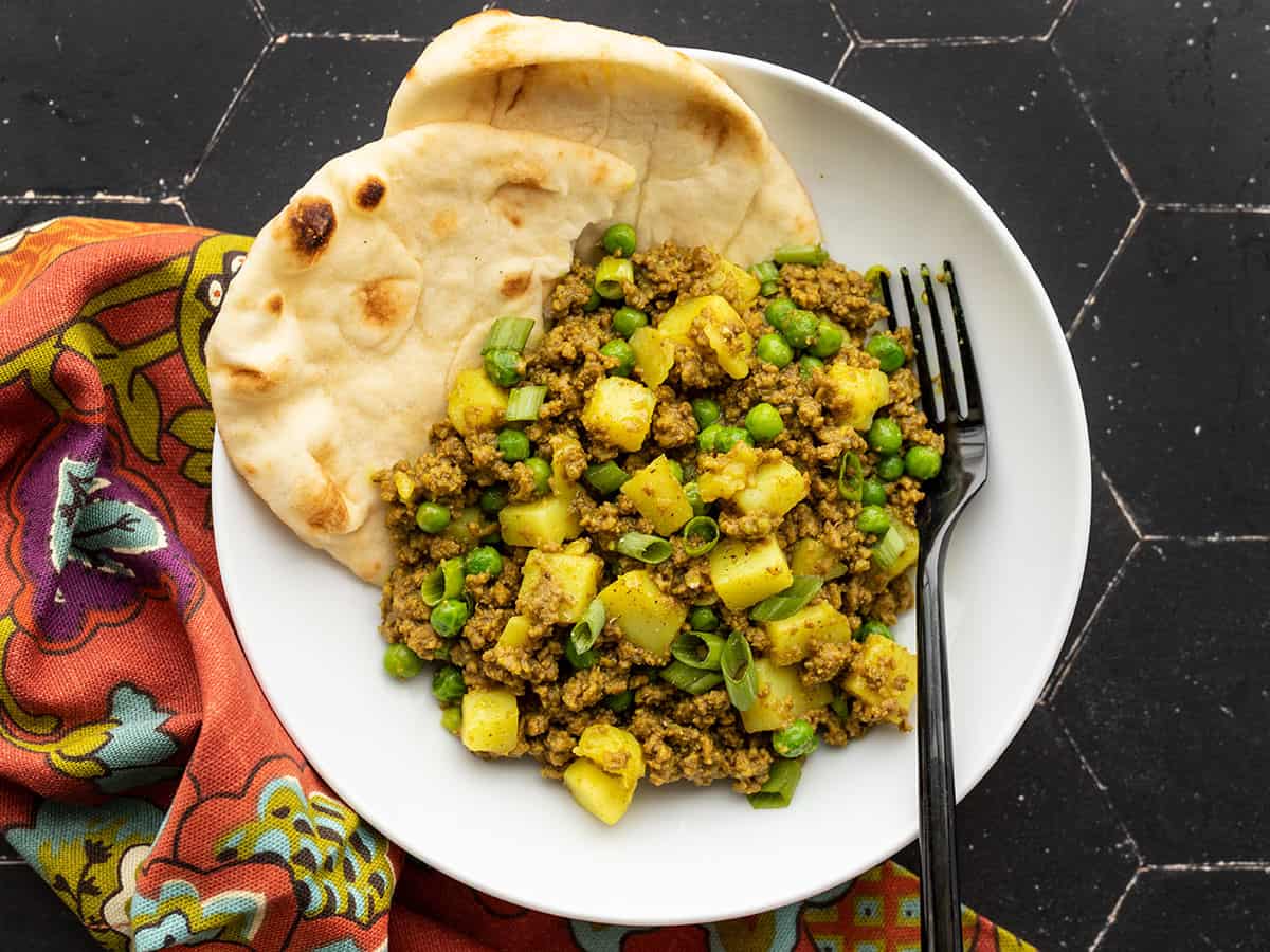 curried ground beef with peas and potatoes in a bowl with naan in the side