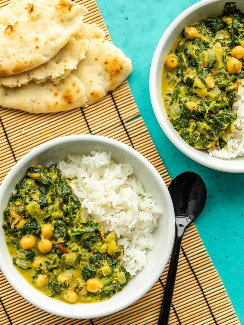 Chana saag is a creamy chickpea and spinach curry that comes together quickly, is full of warm spices, filling, and vegan! Perfect for meal prep! BudgetBytes.com Two bowls of chana saag with rice next to a torn pieces of naan