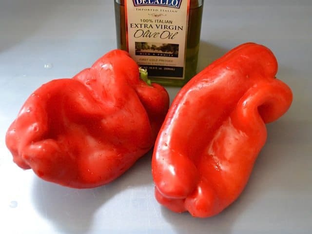 Two red bell peppers and a bottle of olive oil