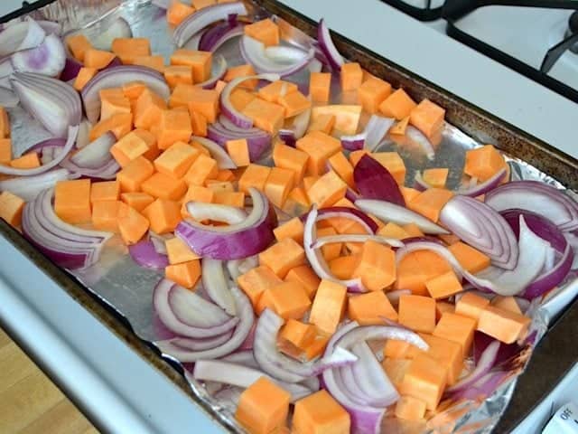 sweet potato and onion on baking sheet lined with tin foil, ready to roast