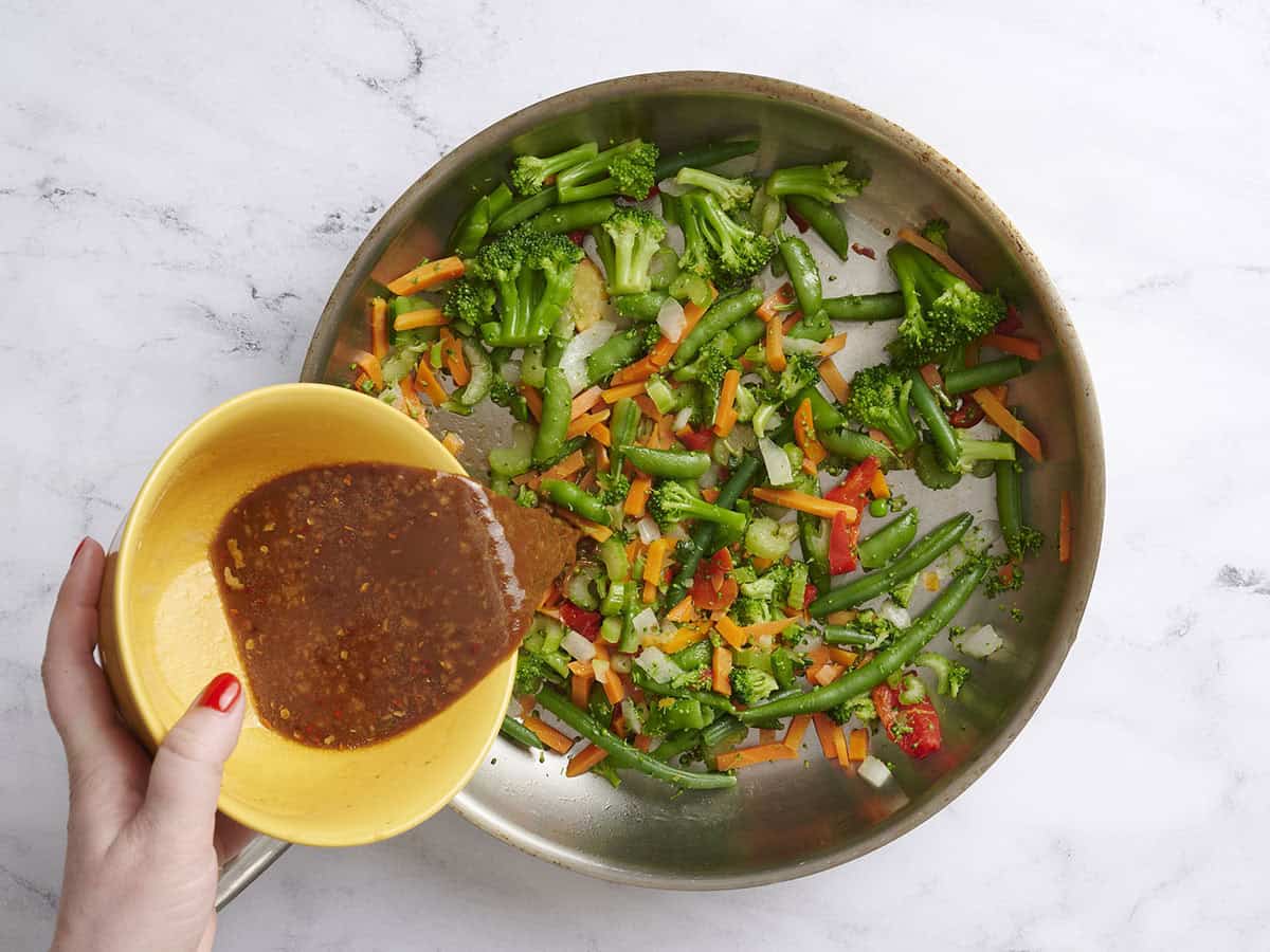 Teriyaki sauce being poured into a skillet of mixed vegetables.