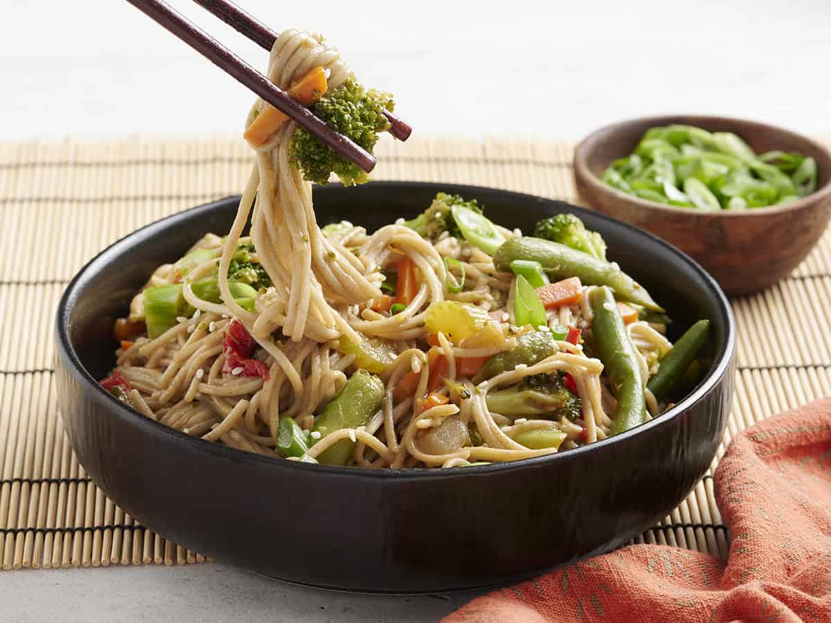 Side view of a bowl of teriyaki noodles in a bowl with chopsticks taking some.