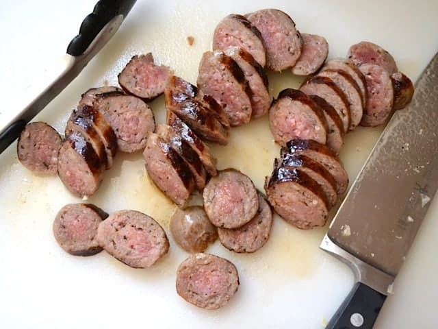 Cooked sausage taken out of pot and sliced with knife