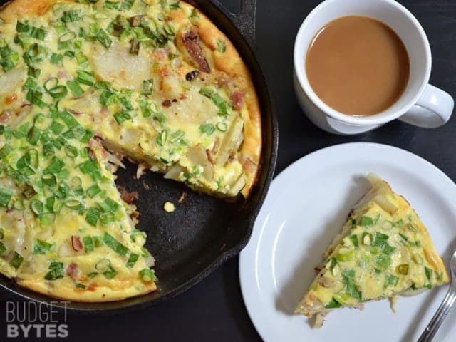Ham and Potato Frittata slice on a plate with a cup of coffee and the rest of frittata in background