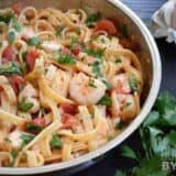 A skillet of spicy shrimp pasta garnished with herbs.