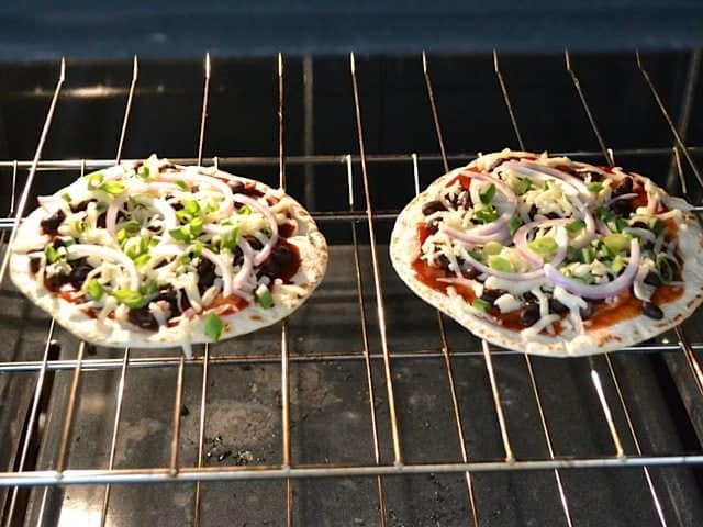 two pizzas baking on wire rack in oven