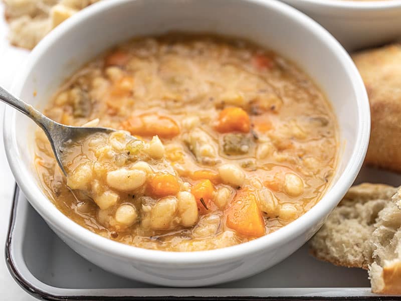 This Slow Cooker White Bean Soup practically makes itself! Just throw everything into the pot and press go for a thick, flavorful, and filling vegan soup. BudgetBytes.com Close up of a spoon lifting a bite of slow cooker white bean soup out of a bowl