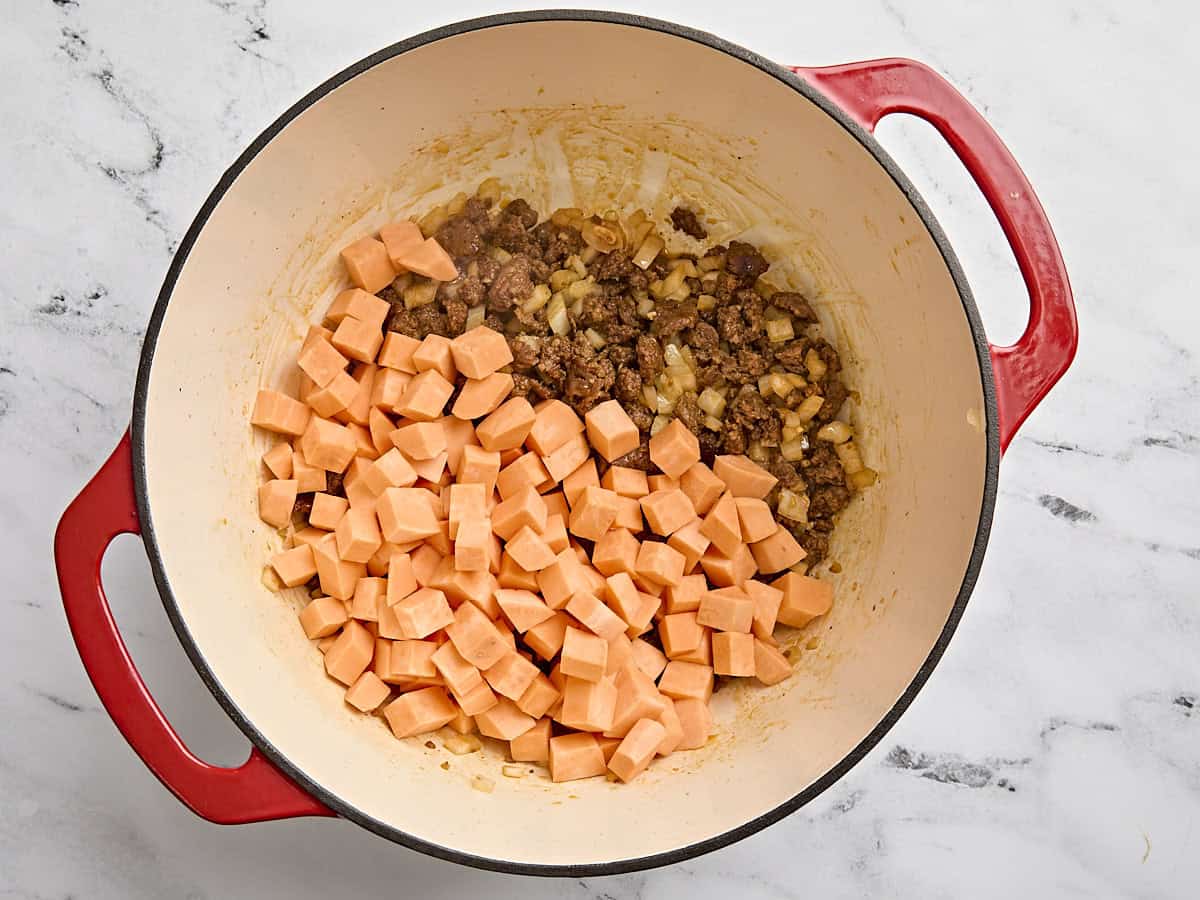 Diced sweet potato added to cooked chorizo and onions in a pot.