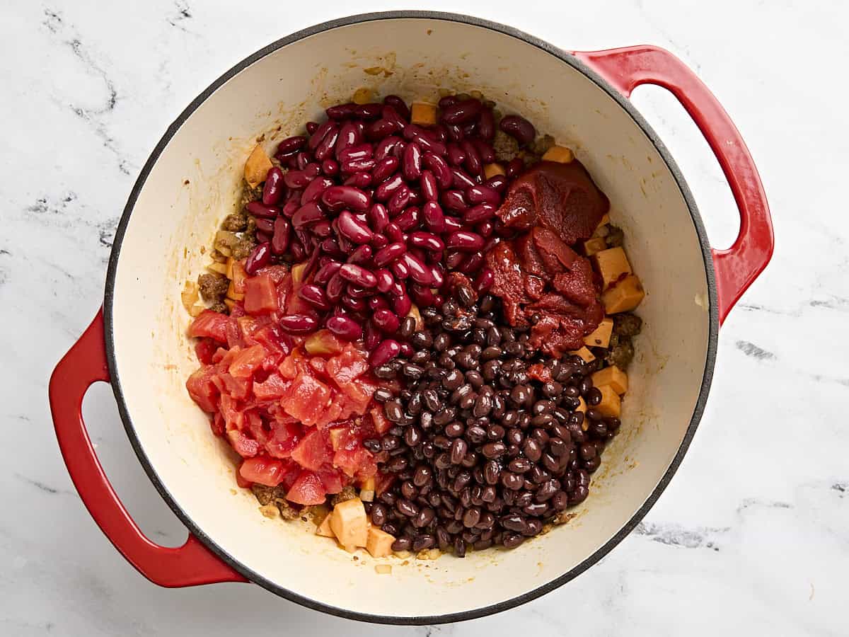 Canned black beans, diced tomatoes, tomato paste, and kidney beans added to a pot with chorizo and sweet potatoes.