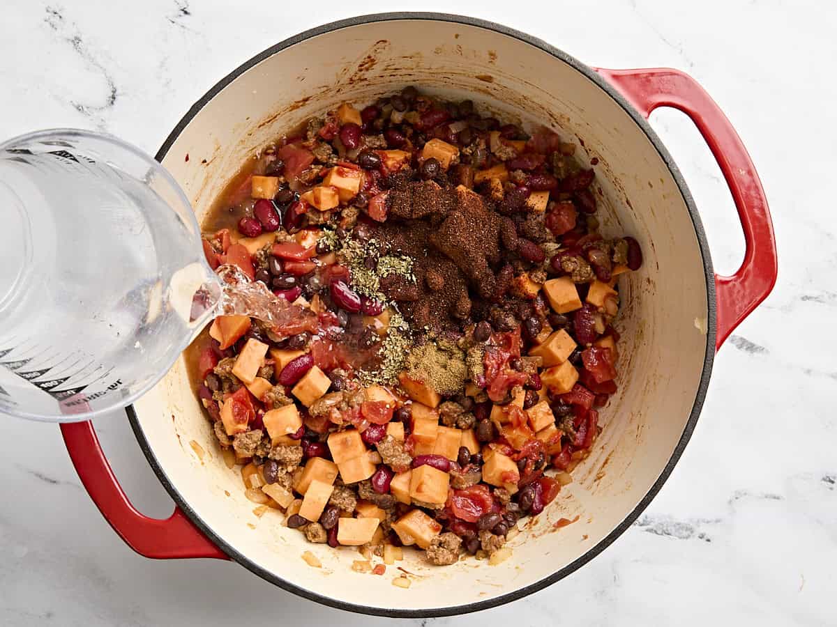 Seasonings and water being added to chorizo sweet potato chilli in a pot.