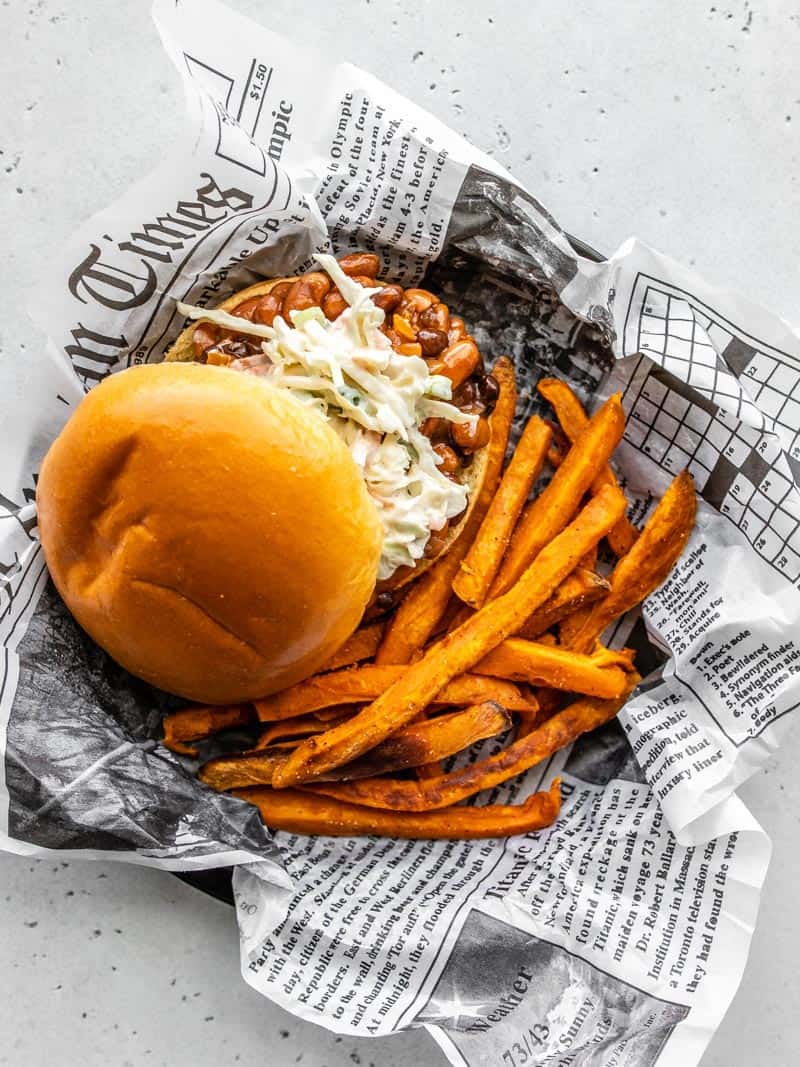 Overhead view of a plate covered with newsprint with one BBQ Bean Slider and some sweet potato fries