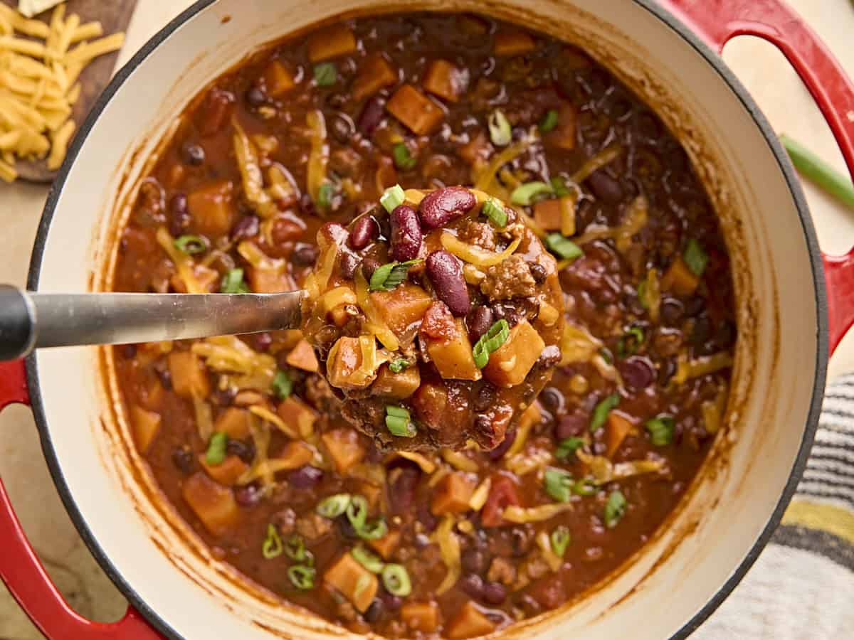Overhead view of a pot of chorizo sweet potato chili with a serving spoon taking some.
