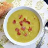 A bowl of split pea and potato soup with bacon served with bread.