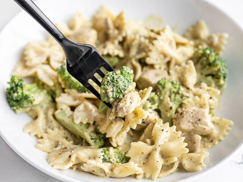A super fast creamy pesto sauce drenches tender pasta, chicken breast, and broccoli for an easy weeknight dinner. Budgetbytes.com Front view of a bowl of creamy pesto pasta with chicken and broccoli, a fork lifting one bite
