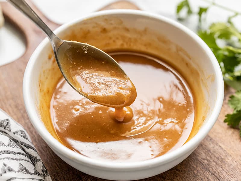 This Peanut Lime Salad dressing is sweet, savory, tangy, and creamy all in one! Drizzle over salad, grilled chicken, shrimp, or vegetables. Budgetbytes.com Front view of peanut lime dressing dripping off a spoon into a bowl.