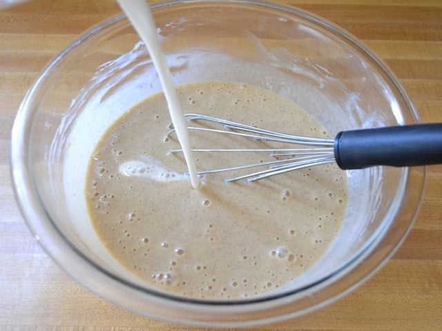 Milk being poured into other ingredients in mixing bowl with whisk
