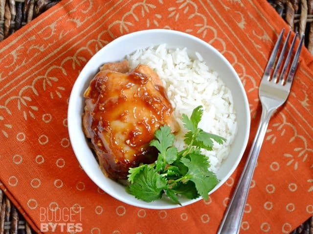 Top view of a bowl with one Honey Sriracha Chicken Thigh over rice, garnished with cilantro. Fork on the side