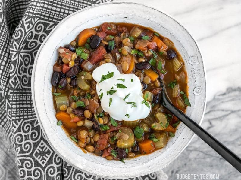 Dollop of sour cream on top of a bowl of Chunky Lentil and Vegetable Soup with a spoon