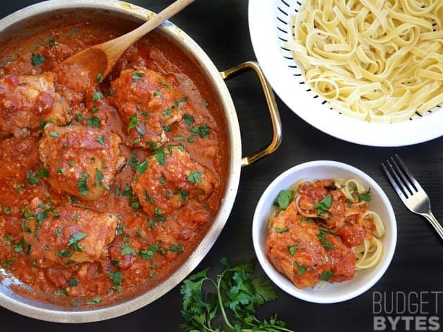 Top view of a pan of Chicken Arrabbiata, a colander of cooked noodles and a bowl of chicken over noodles ready to eat