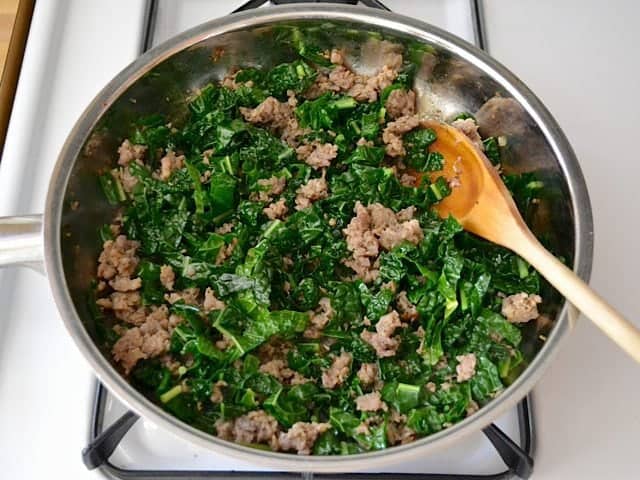chopped kale added to cooked sausage in skillet