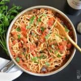 A skillet of pasta topped with eggplant sauce.