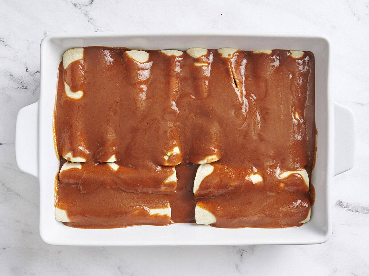 Beef enchiladas in a baking dish topped with enchilada sauce.