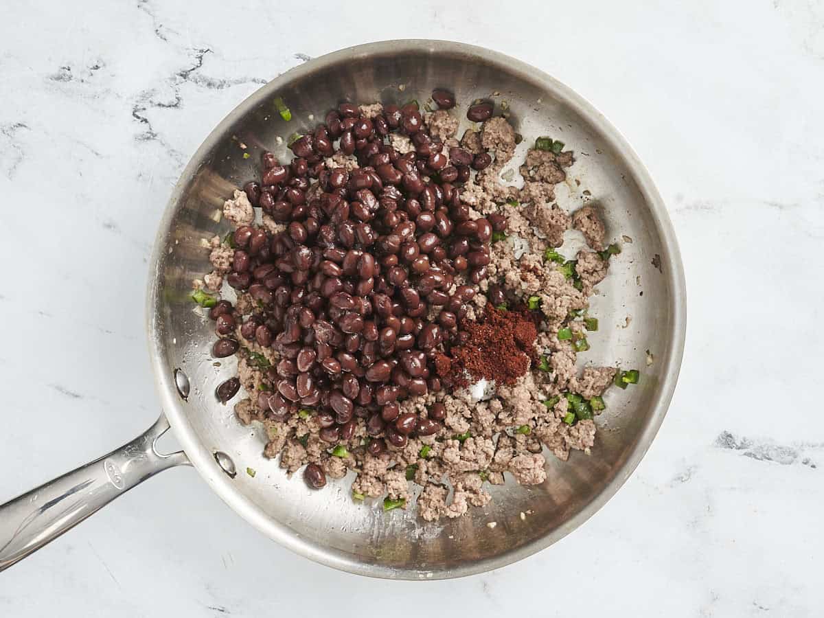 Black beans and chili powder added to a skillet of browned beef.