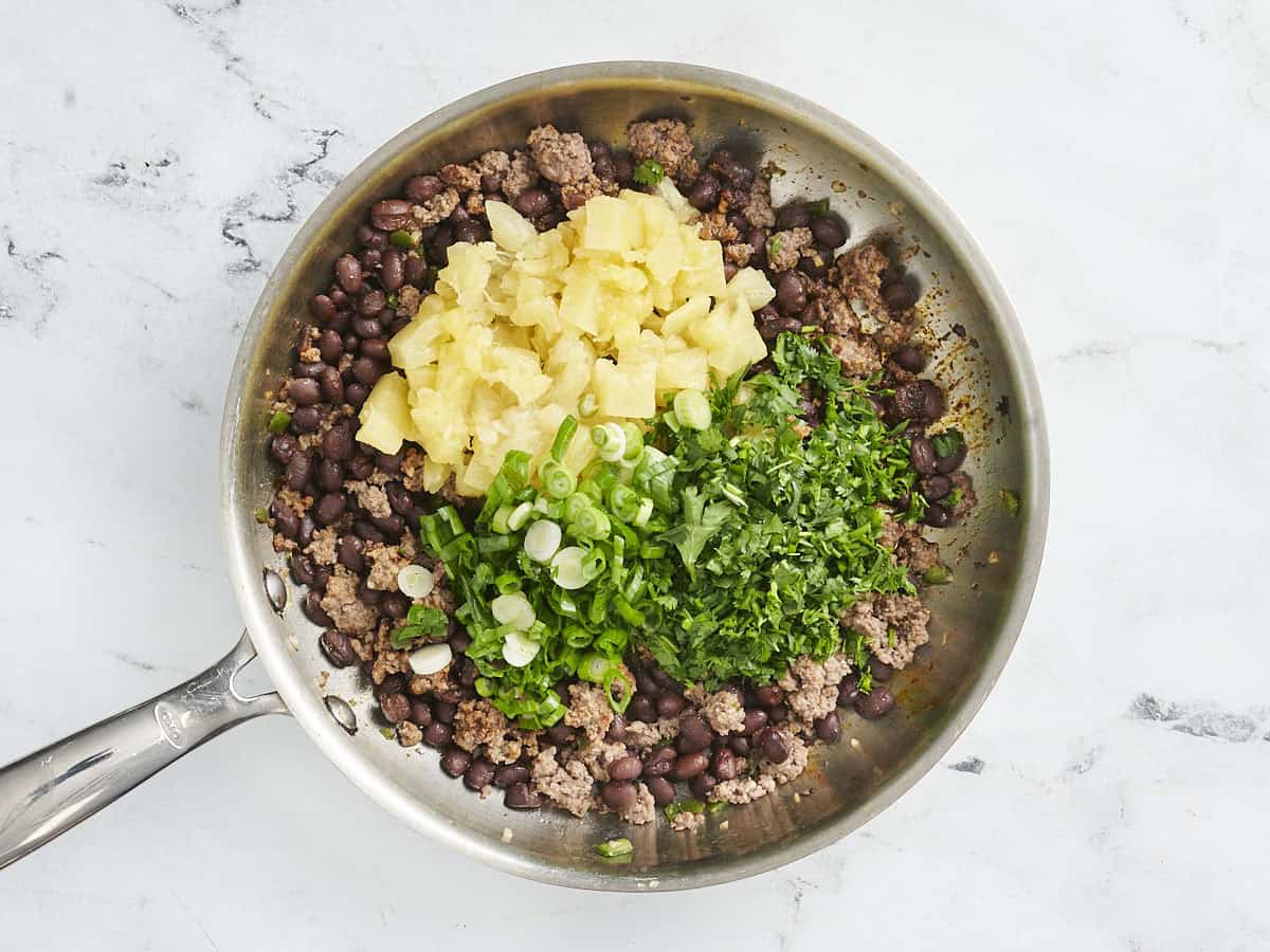 Canned pineapple, green onions, and cilantro added to ground beef and black beans in a skillet.