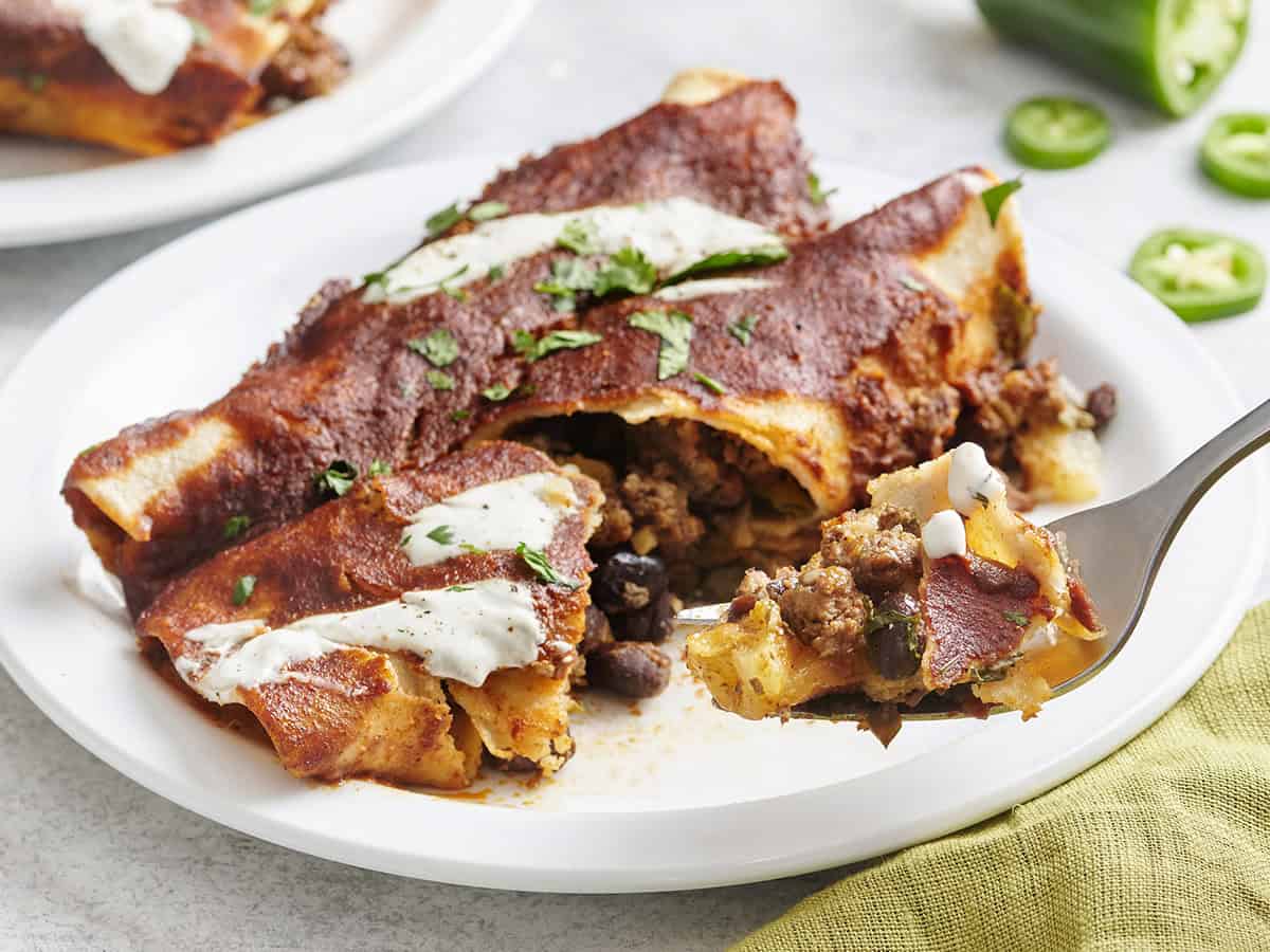 Two homemade beef enchiladas on a plate with a fork taking some.