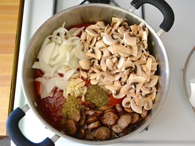 Tomato sauce and vegetables added to browned sausage in pot