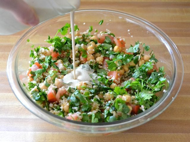 Dressing being poured over salad in mixing bowl