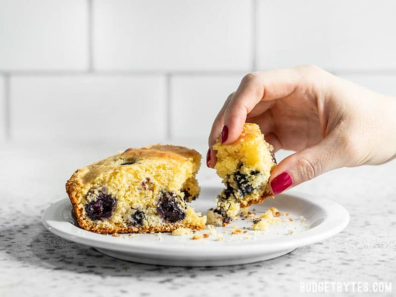 For a deliciously lazy weekend treat, whip up this super fast and easy Lemon Blueberry Cornbread Skillet. Great for breakfast, dessert, or coffee! Budgetbytes.com A hand taking a piece of Lemon Blueberry Cornbread from a plate.