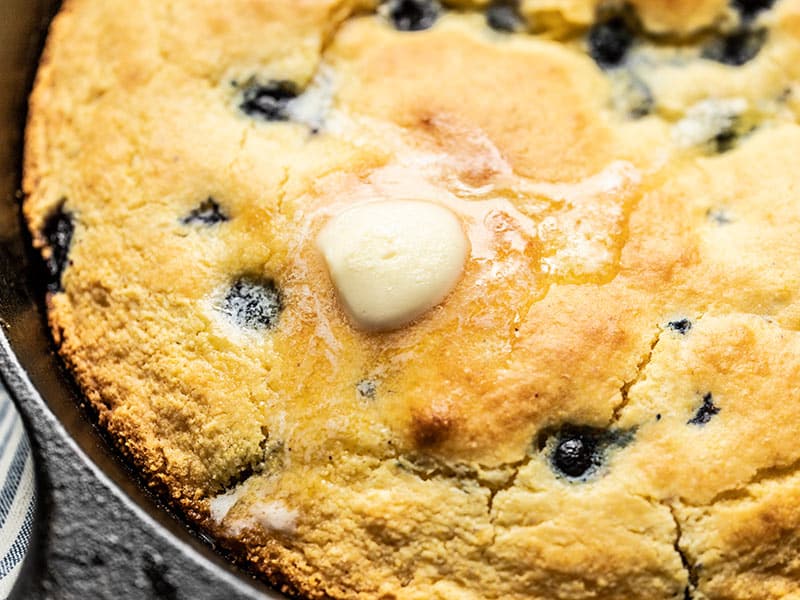 For a deliciously lazy weekend treat, whip up this super fast and easy Lemon Blueberry Cornbread Skillet. Great for breakfast, dessert, or coffee! Budgetbytes.com Close up of a pat of butter melting on the surface of Lemon Blueberry Cornbread