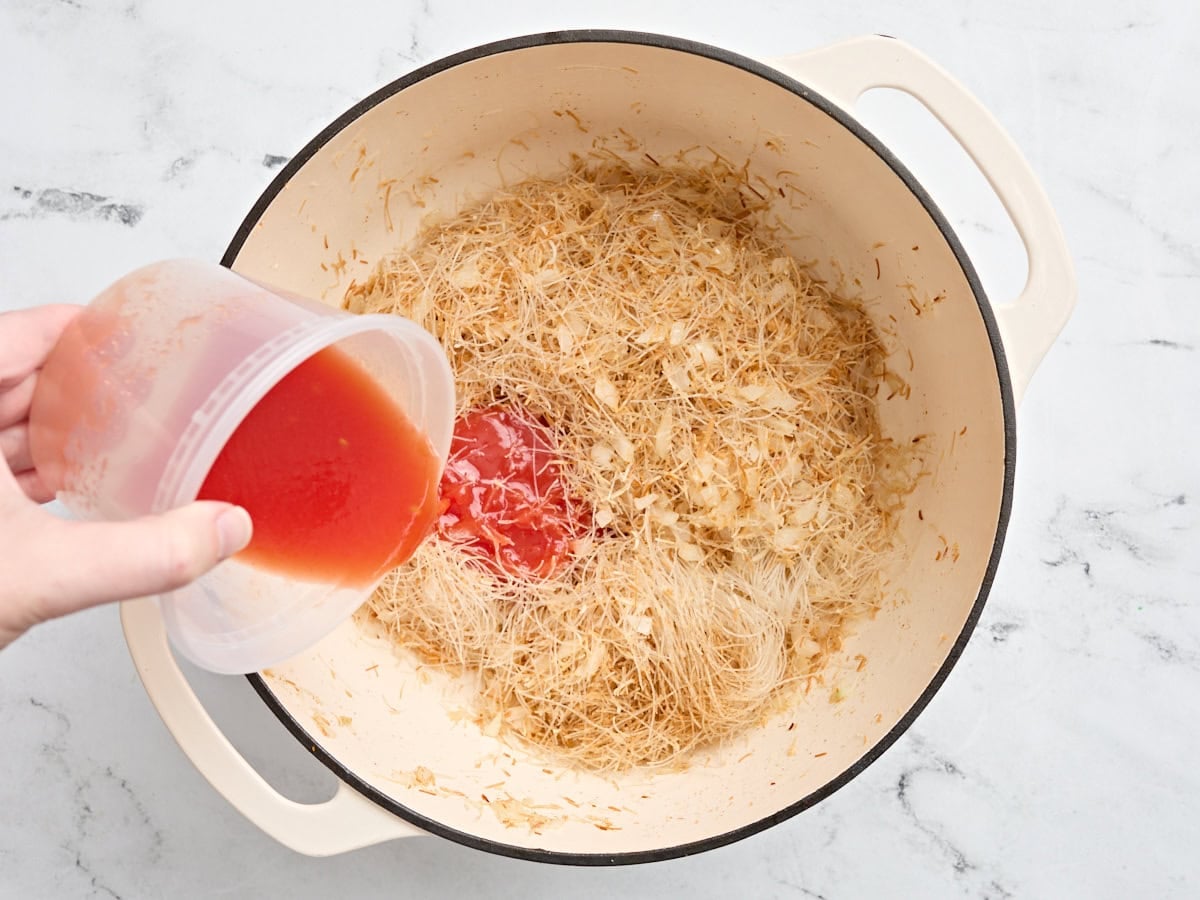 Canned tomato juice added to a pot of toasted noodles and diced onion.