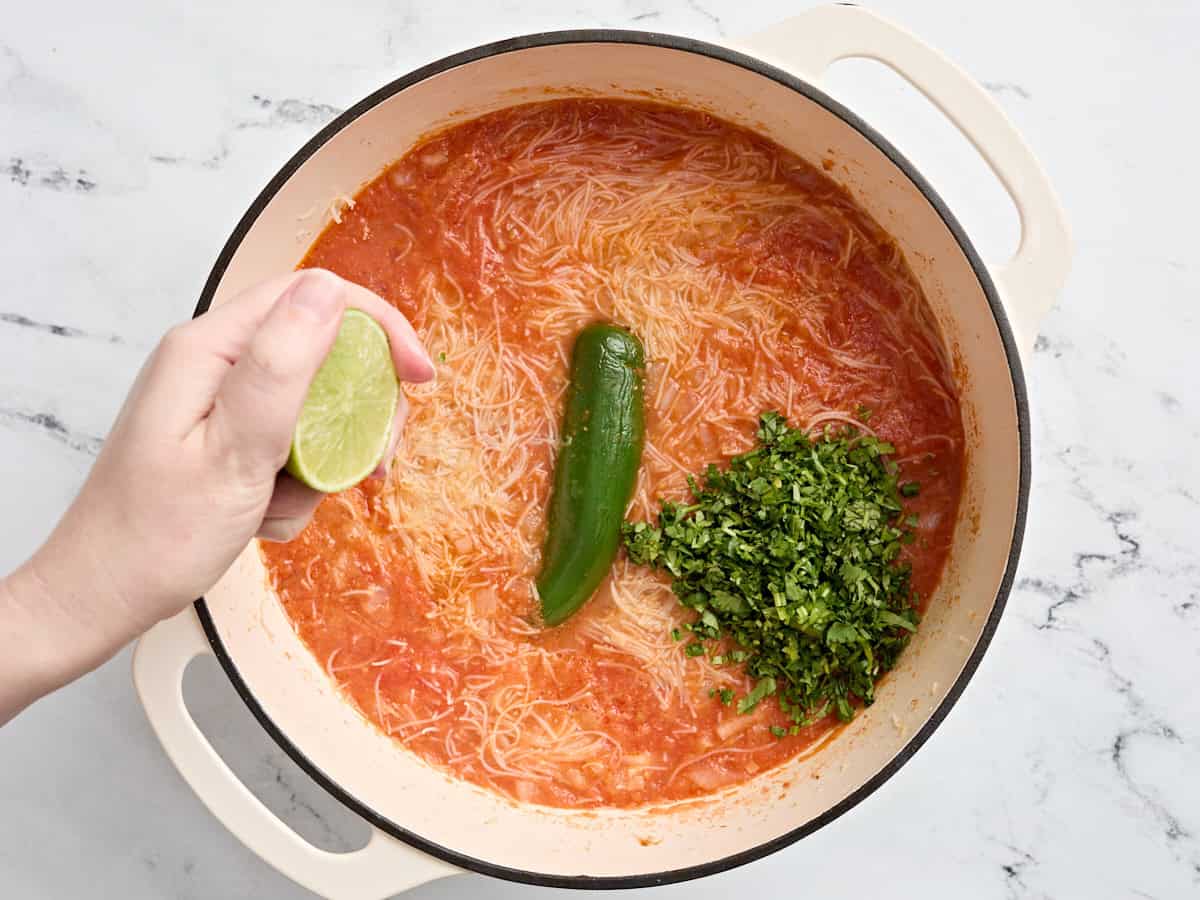 Chopped cilantro and half a lime being squeezed into pot of sopa de fideo.