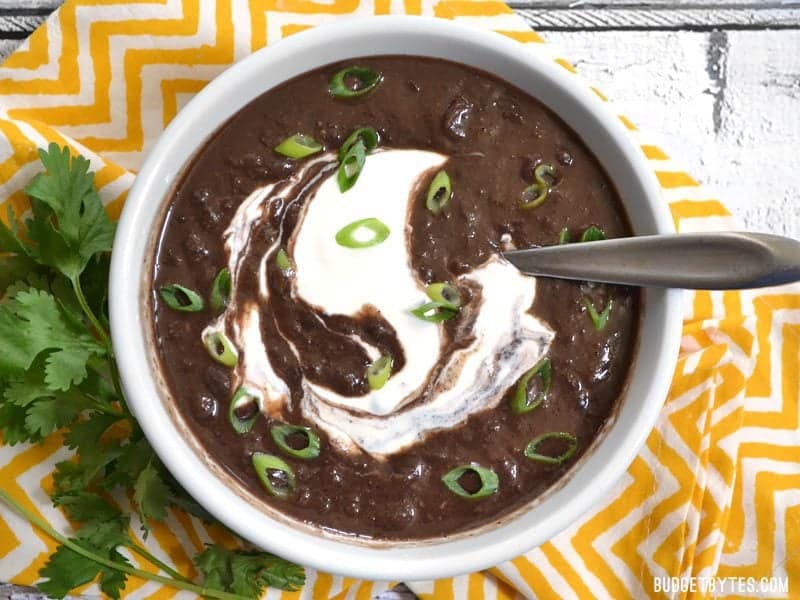 top view of a bowl of black bean soup garnished with green onion and sour cream