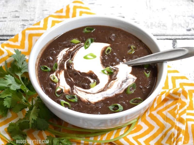 Side view of a bowl of black bean soup garnished with green onion and sour cream